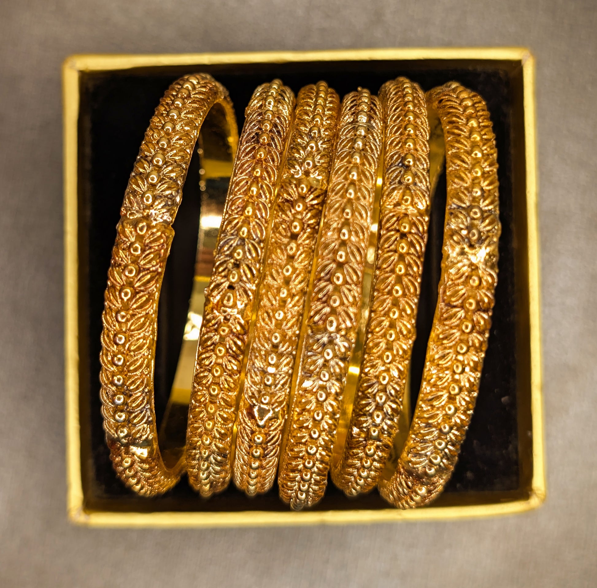 Set of gold bangles in a decorative box on a gray background super top angle