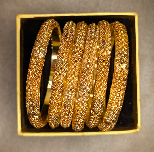 Set of gold bangles in a decorative box on a gray background super top angle