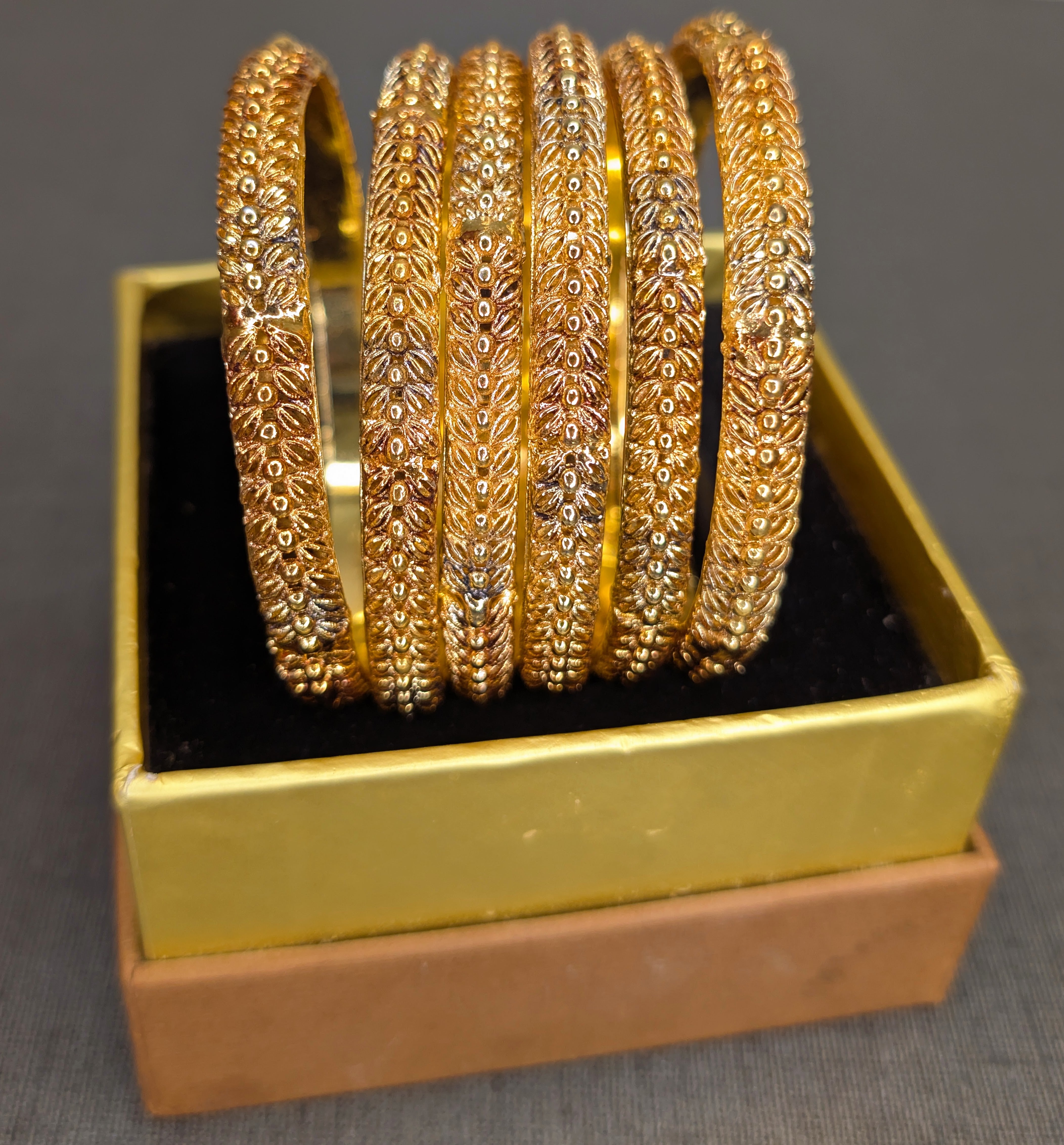 Set of gold bangles in a gold box on a gray background