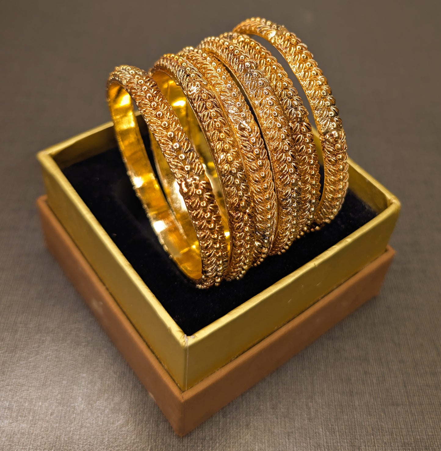 Set of gold bangles in a gold box on a gray background from tilt angle to capture
