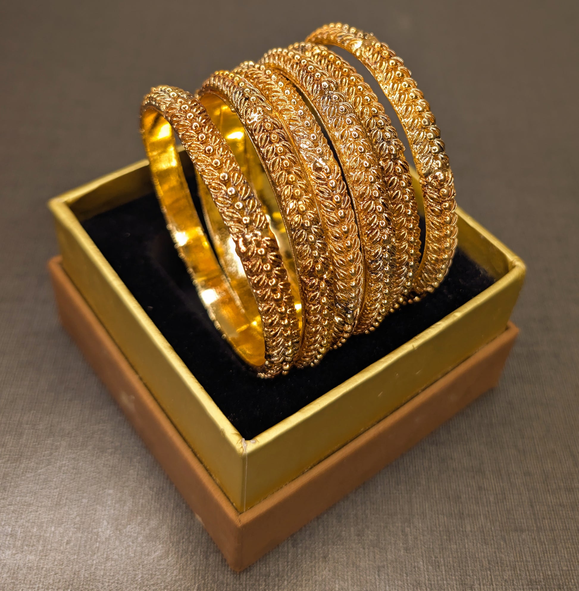 Set of gold bangles in a gold box on a gray background from tilt angle to capture