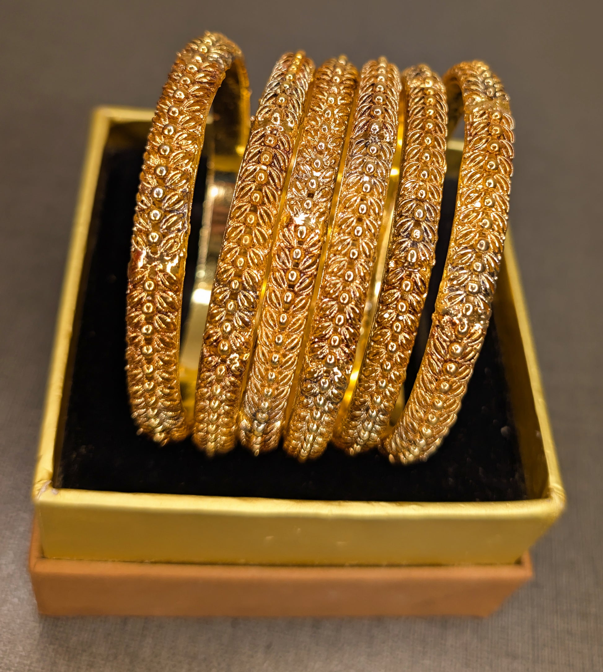 Set of gold bangles in a gold box on a gray background  from top angle