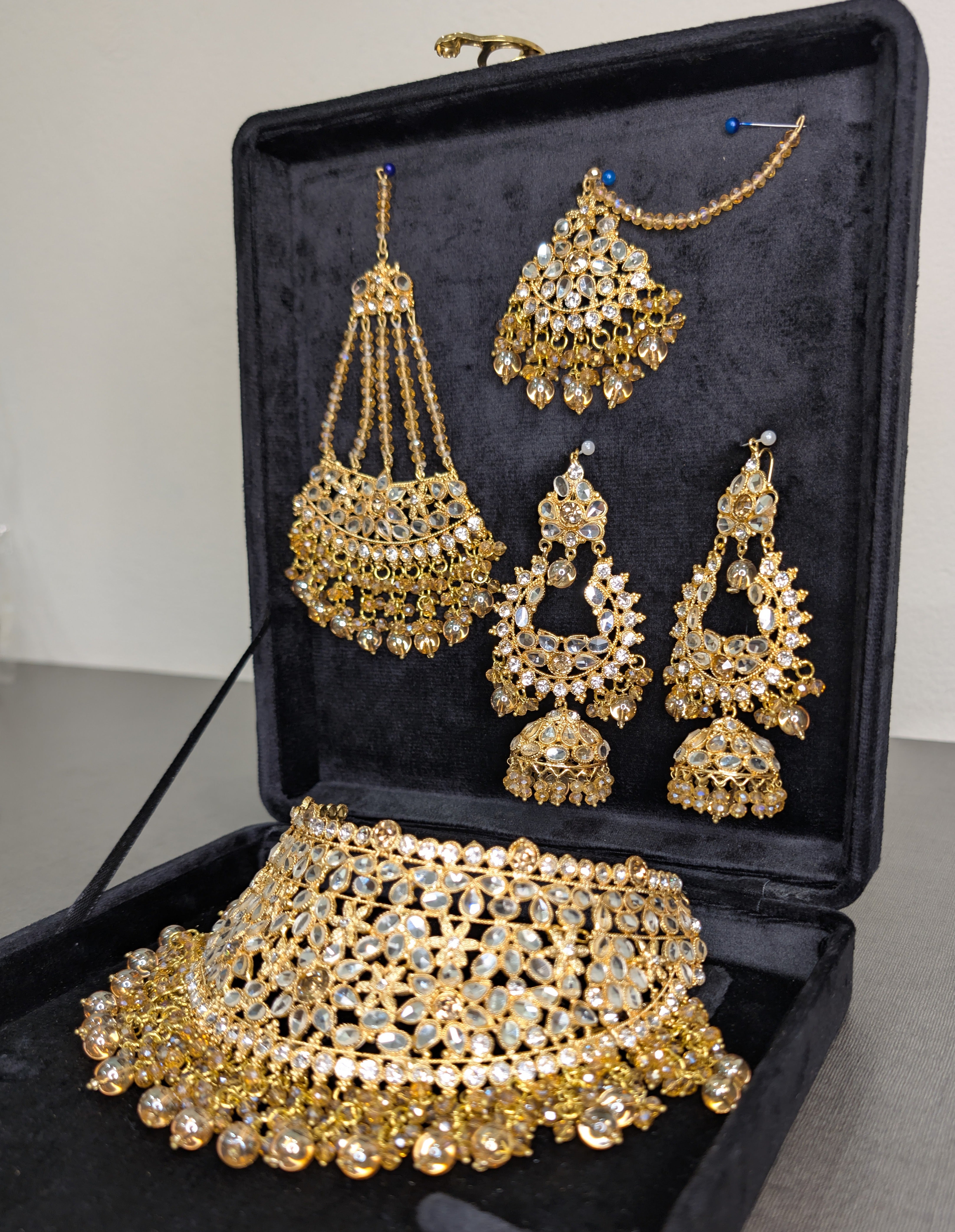 Set of gold jewelry including necklace, earrings, and choker in a black jewelry box.