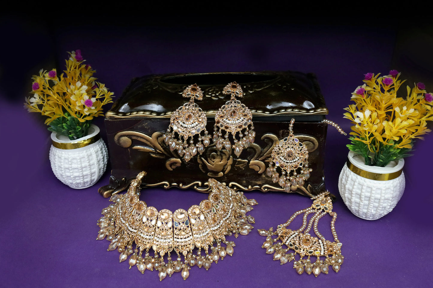 Set of gold jewelry including necklace, earrings, and choker on a purple background with decorative vases.