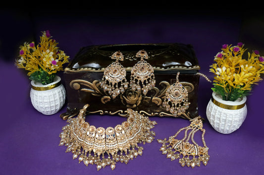 Set of gold jewelry including necklace, earrings, and choker on a purple background with decorative vases.