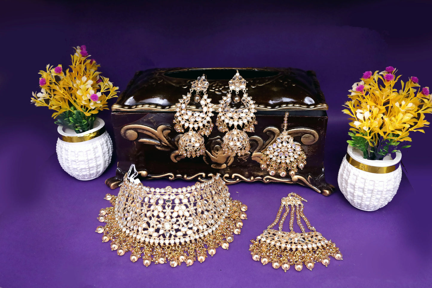 Set of gold jewelry including necklaces and earrings on a purple background with decorative vases.
