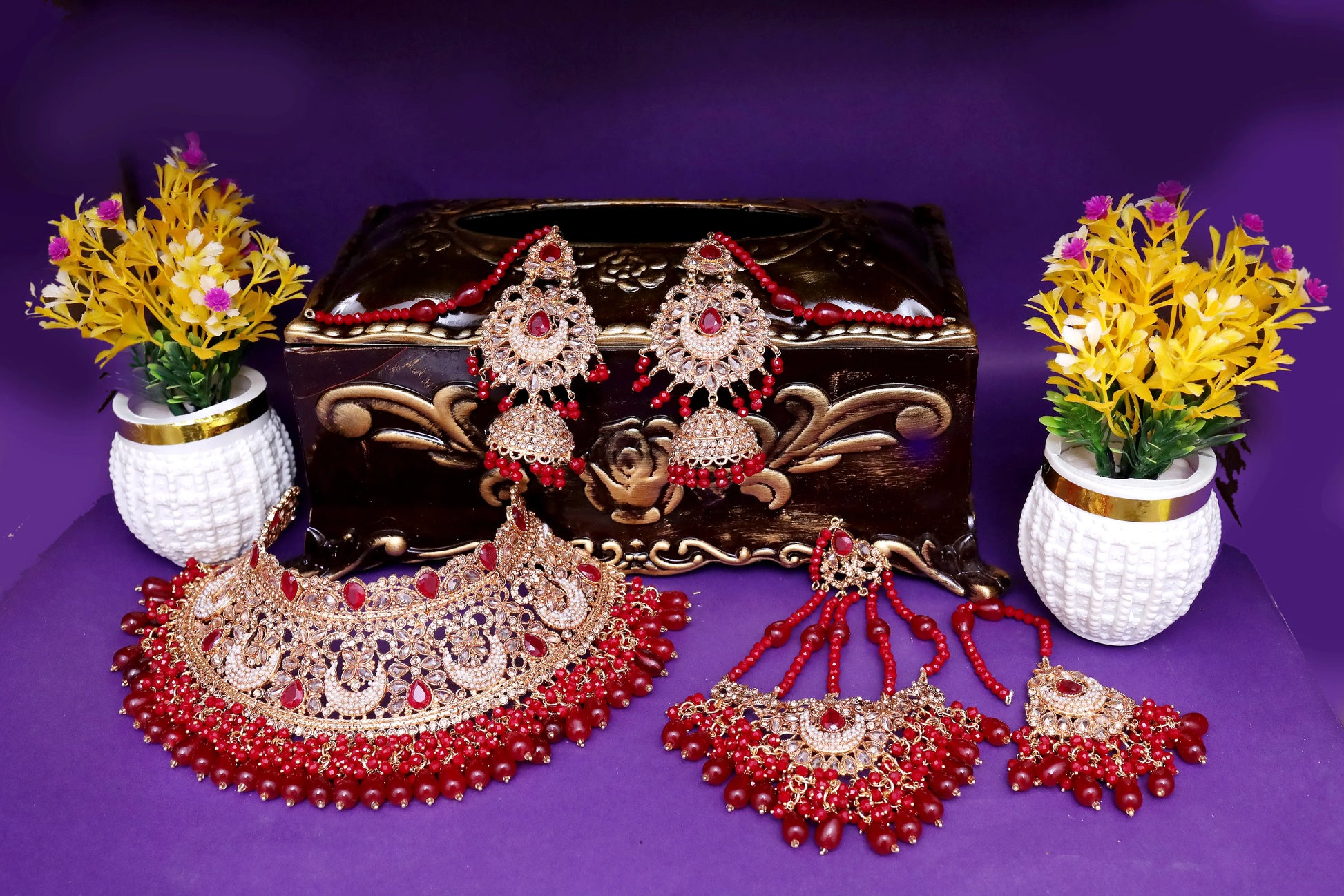 Set of red and gold jewelry on a purple background with decorative plants.