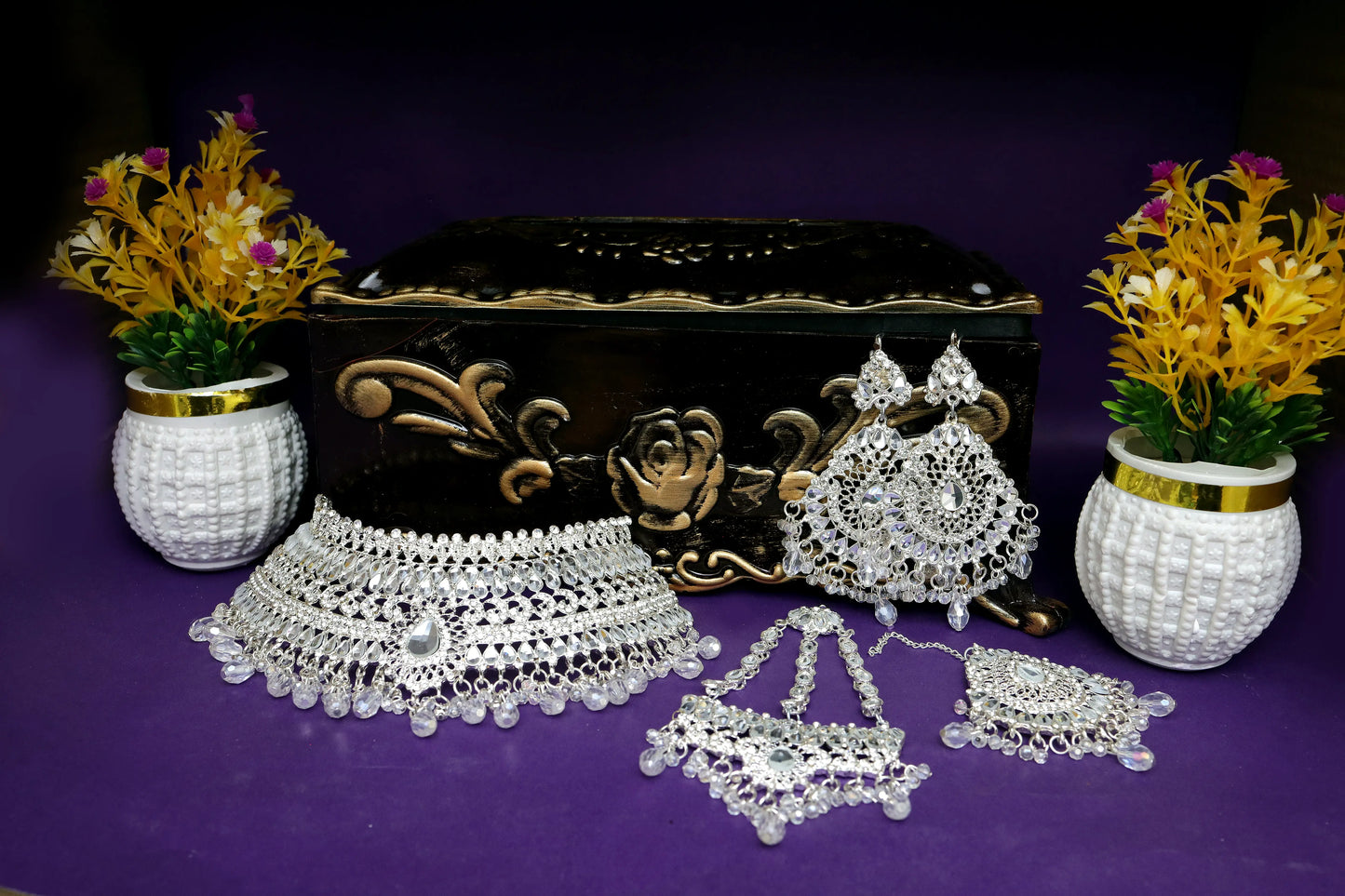 Silver jewelry set with decorative box and flowers on a purple background