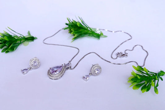 Silver necklace with purple pendant and matching earrings on a light background with green leaves.